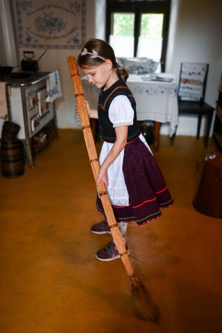 Népviseletbe öltözött kislány a tájházban felsepri a padlót. A fotót a Z'imázs Foto készítette.
